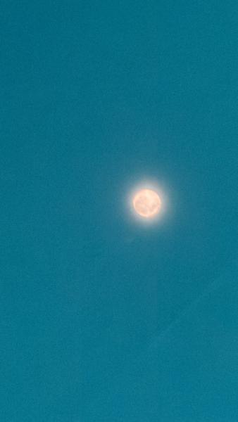The photo captures a luminous celestial body, likely the moon, glowing brightly against a deep teal-blue sky